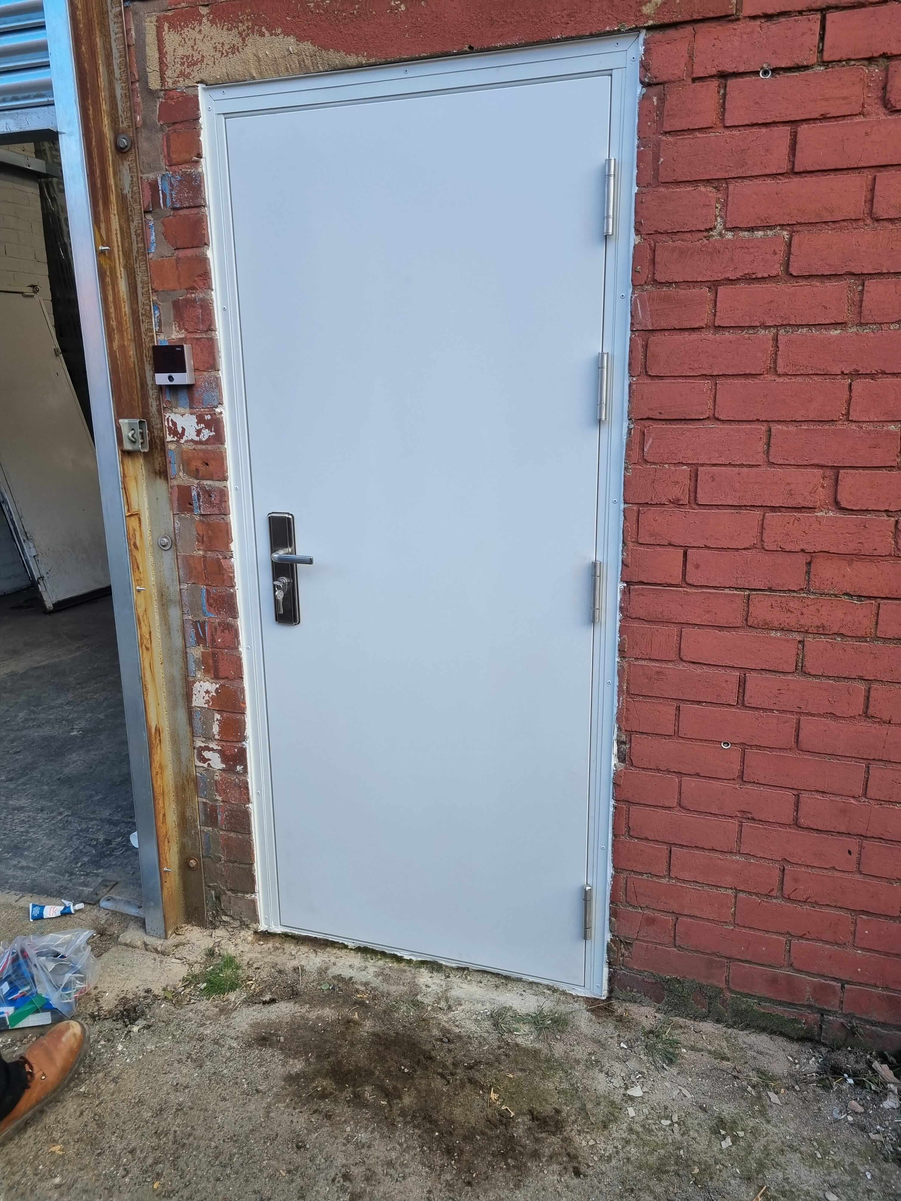 new white ultra security steel door fitted between 2 brick walls.