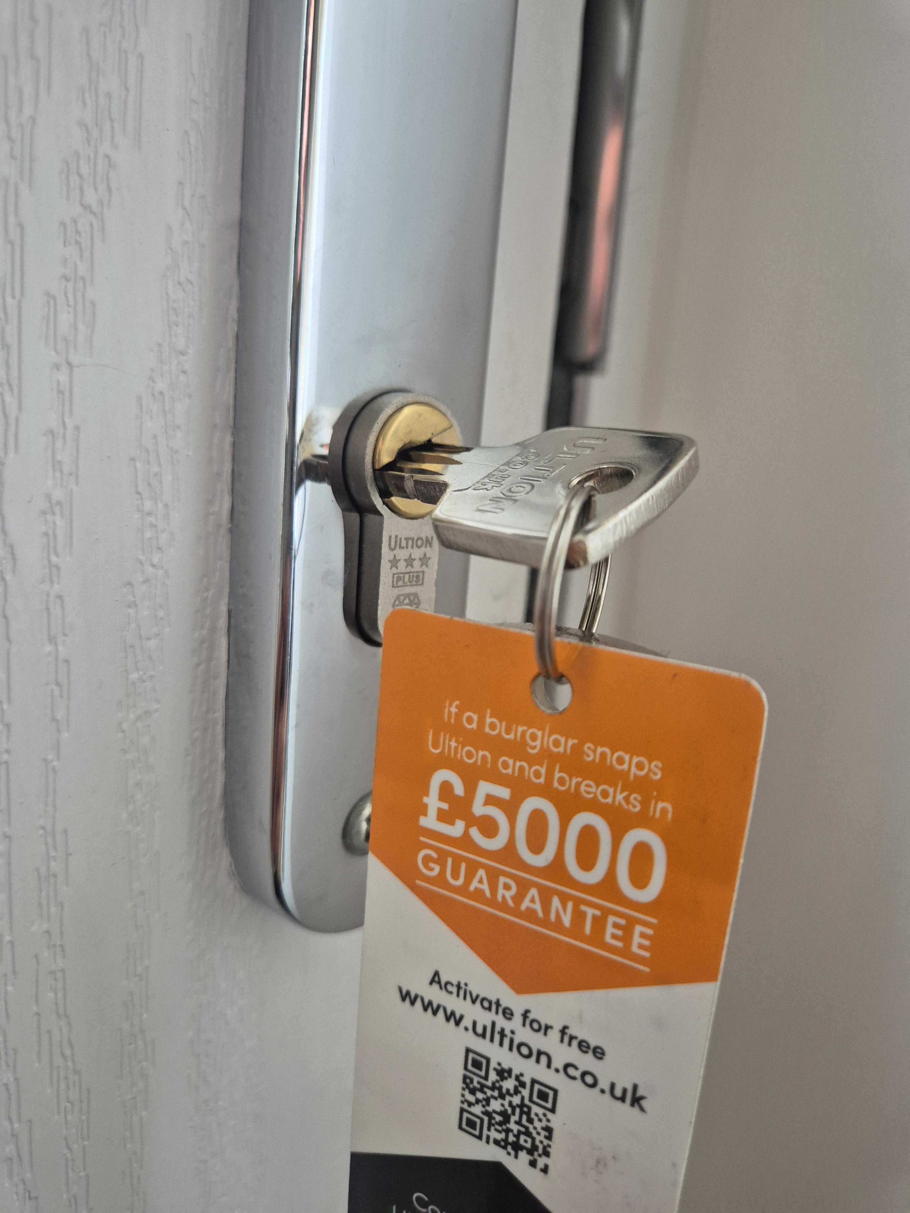 Ultion lock fitted to white coomposite door with chrome door handle showing the £5000 burglary guarantee card and keys