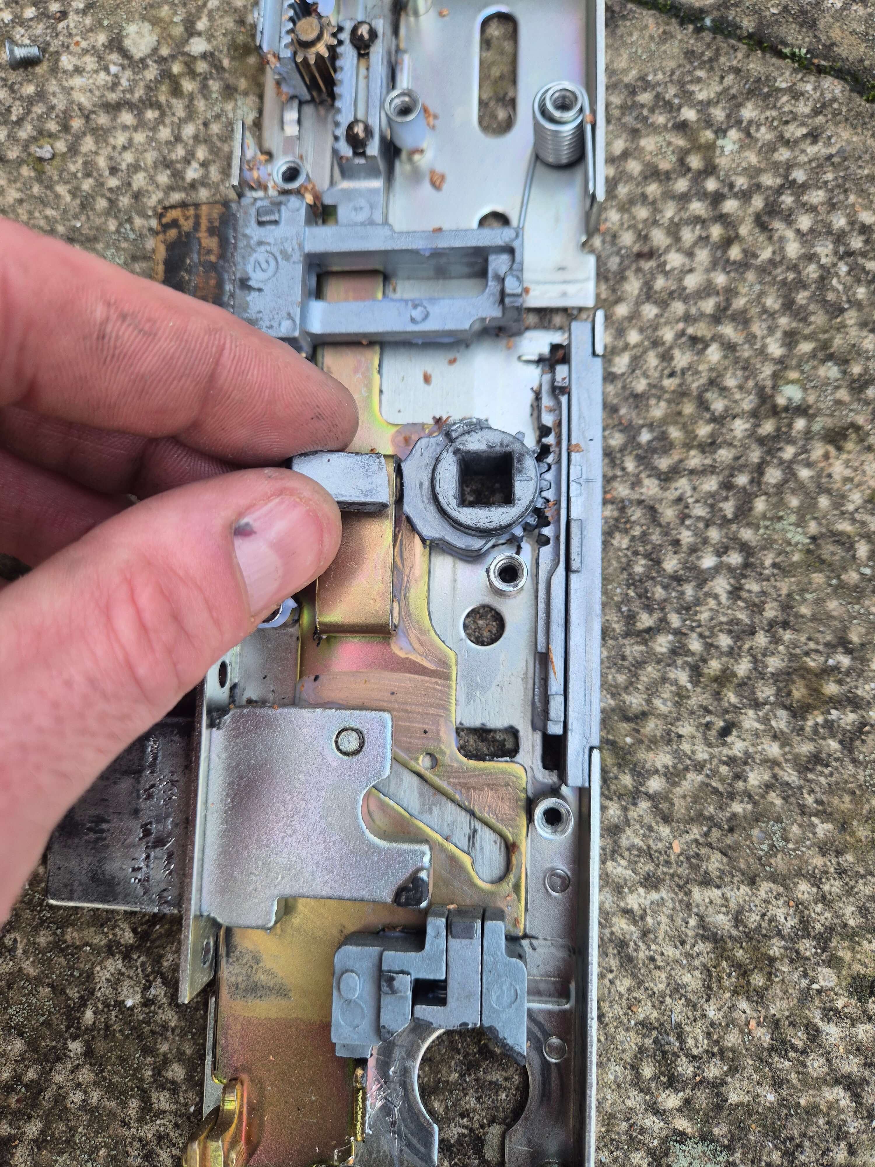 Hand holding broken multipoint lock part inside exposed multipoint lock internals.