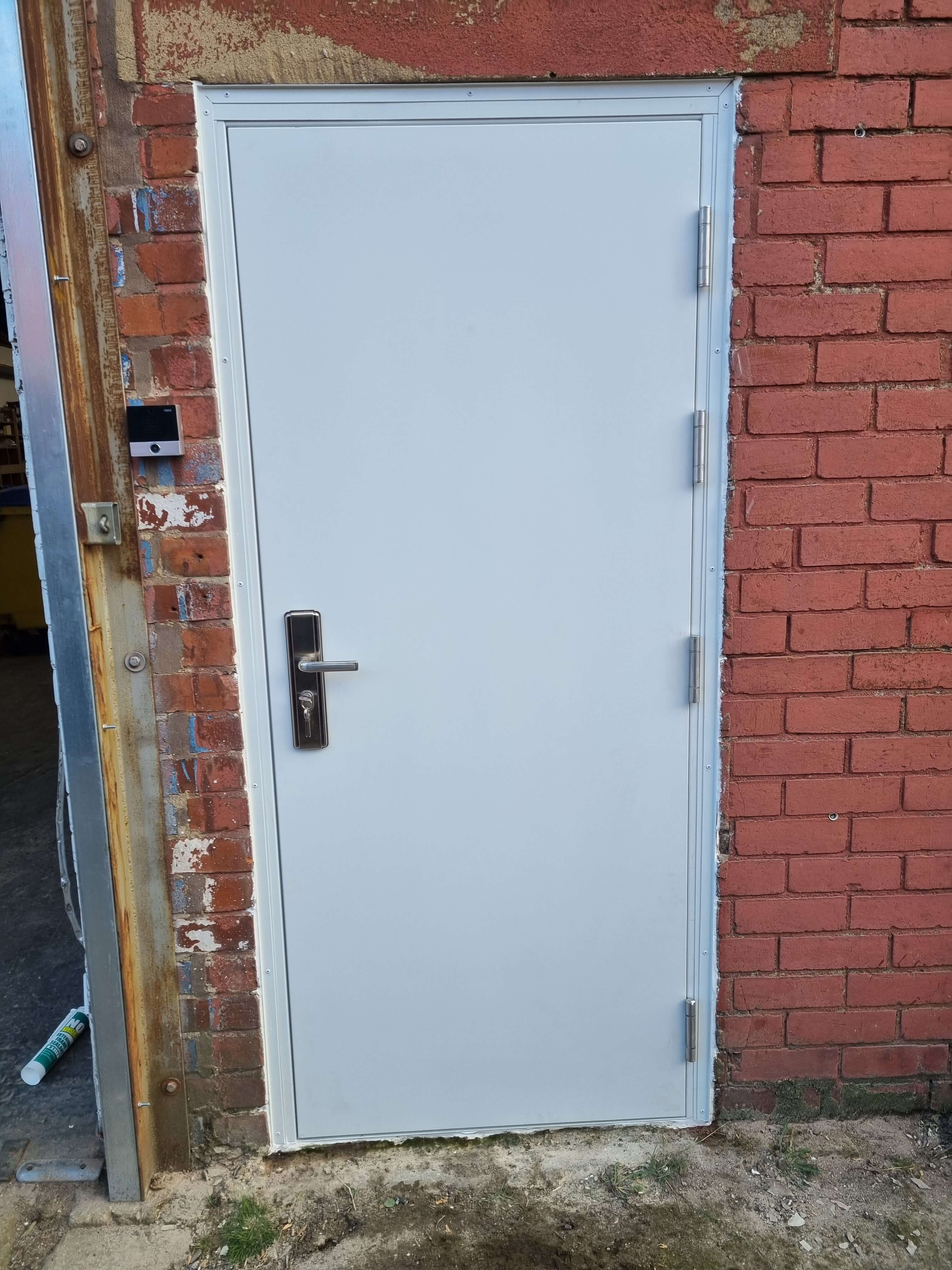 White high security steel door fitted in Leeds between 2 red brick reveals 
